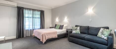 Una habitación de hotel moderna con una cama, un sofá y un ventanal con cortinas.