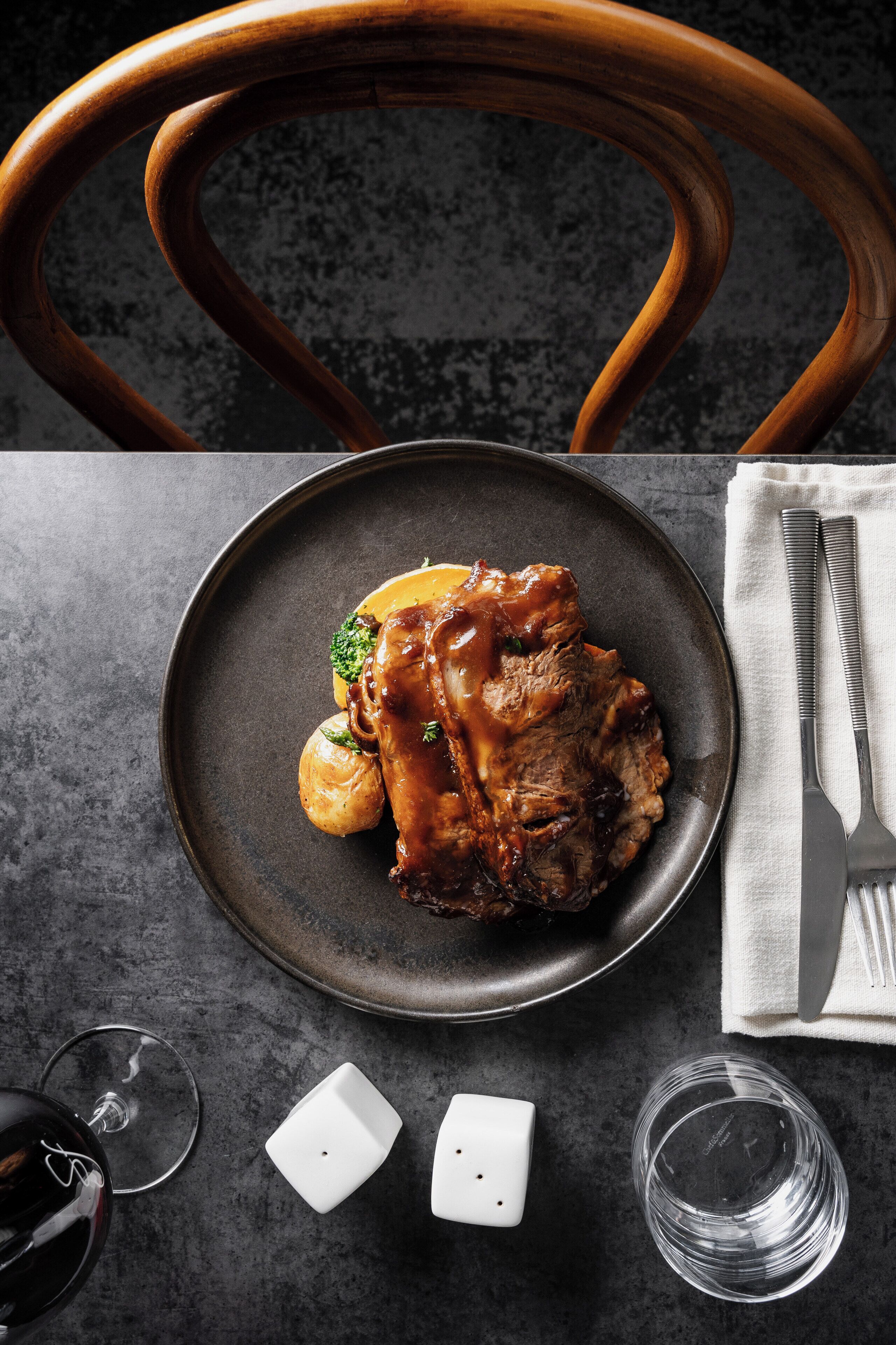 A plate of food with a glass of red wine and salt and pepper shakers on a table.