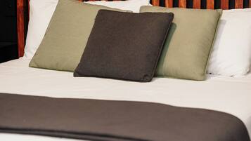 Una cama con cabecera de madera, ropa de cama blanca y tres almohadas de colores diferentes.