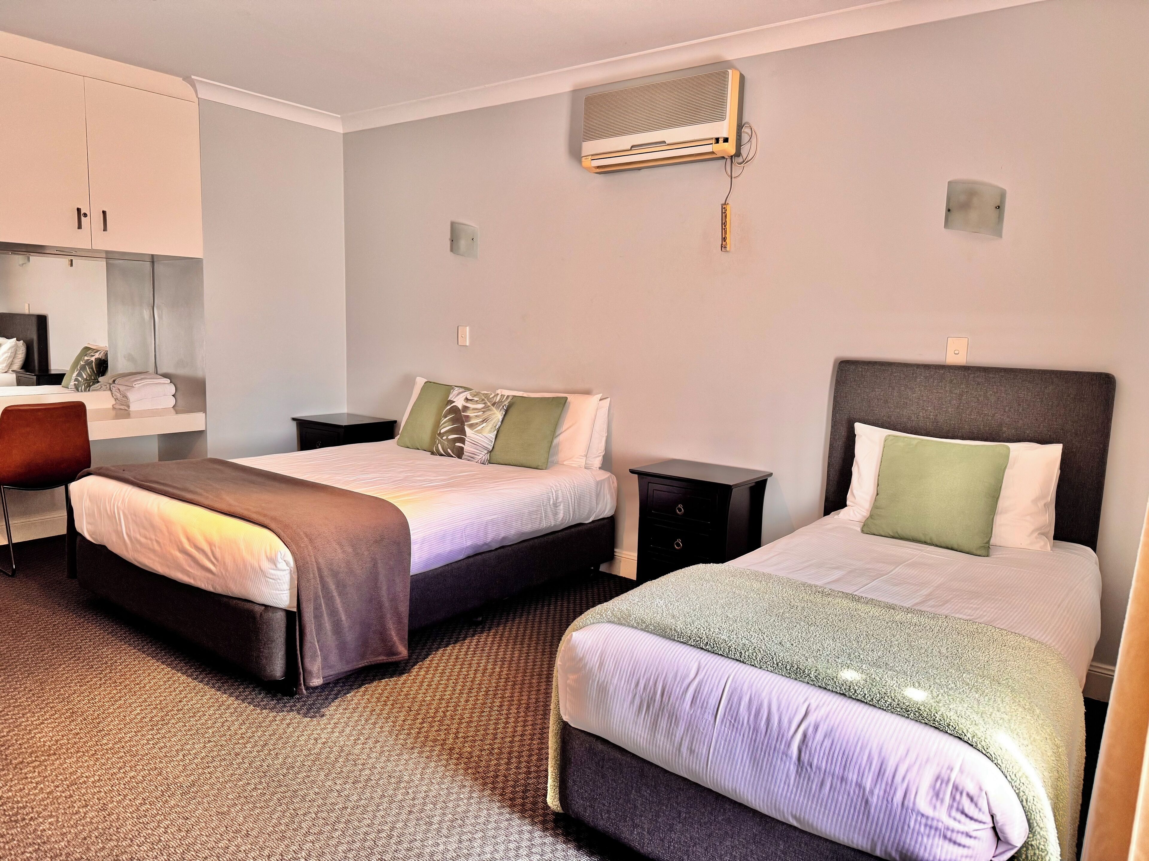 A hotel room with two beds, a desk, a chair, and an air conditioning unit.
