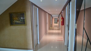 A long, well-lit hallway with doors on both sides, a fire extinguisher on the right, and a framed painting on the left wall. - Beira Mar Hotel (Aracaju)