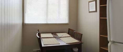 Un comedor con una mesa, sillas, una ventana con persianas y un refrigerador.