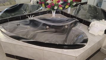 Ein modernes Badezimmer mit einer großen, schwarzen Whirlwanne, weißen Fliesenwänden und einem Spiegel, der den Raum reflektiert.