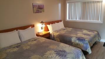 A hotel room with two beds, a nightstand, a lamp, a window with blinds, and a wall-mounted picture.