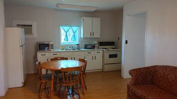 A compact kitchen with white cabinets, a microwave, a stove, and a sink. There's a dining table with chairs and a red sofa in the living area.