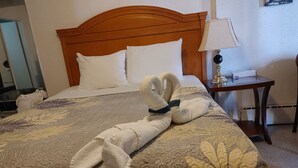 Una cama bien hecha con un edredón estampado con motivos florales, un cabecero de madera y un par de toallas dispuestas sobre la cama.