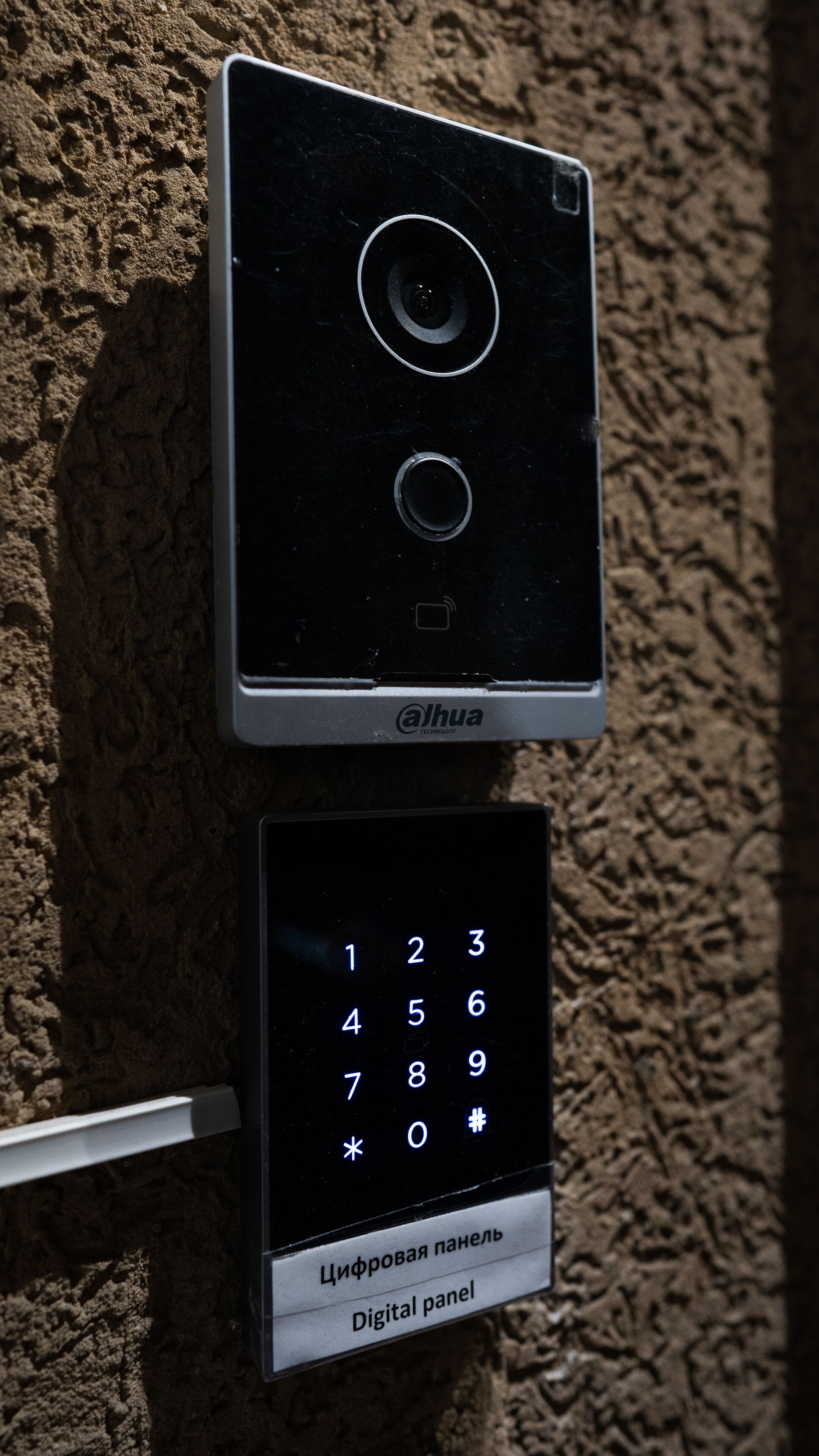 A digital keypad with a numeric keypad and a small screen, mounted on a textured wall.
