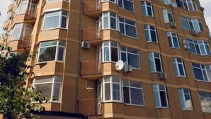 En høj boligbygning med flere altaner, airconditionanlæg og en klar himmel.