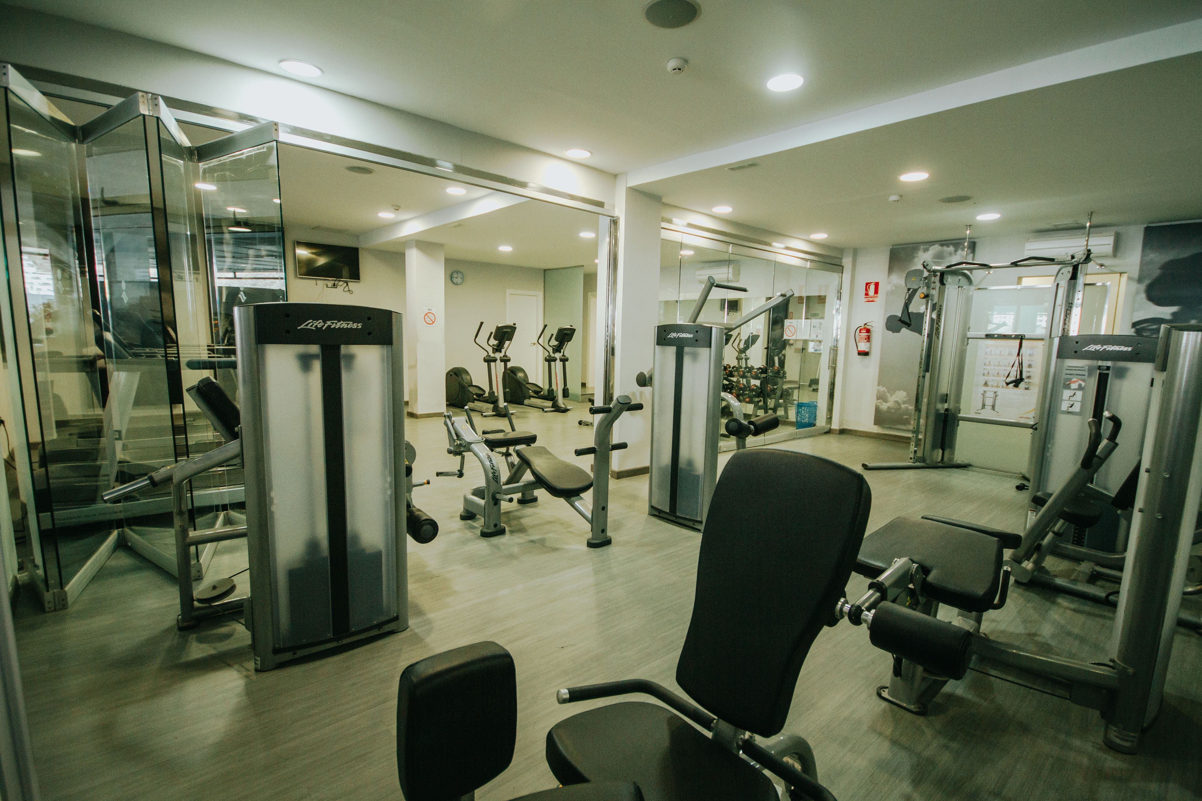 Uma academia com diversos equipamentos de exercício, incluindo esteiras, aparelhos de musculação e pesos livres.
