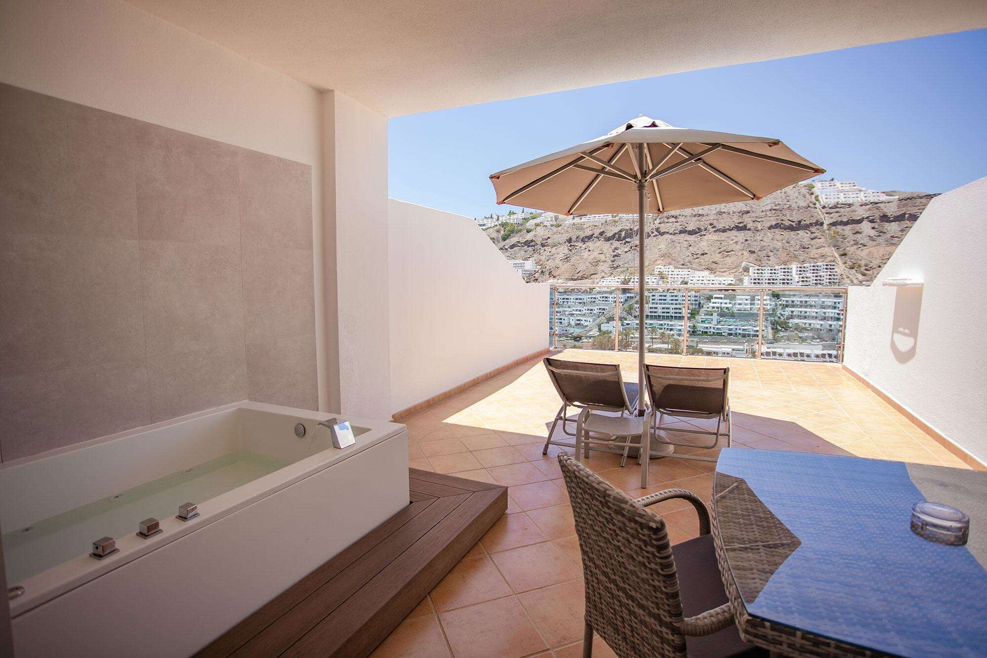 Un balcon avec une baignoire, une table avec des chaises et un parasol.
