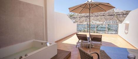 A balcony with a bathtub, a table with chairs, and an umbrella.
