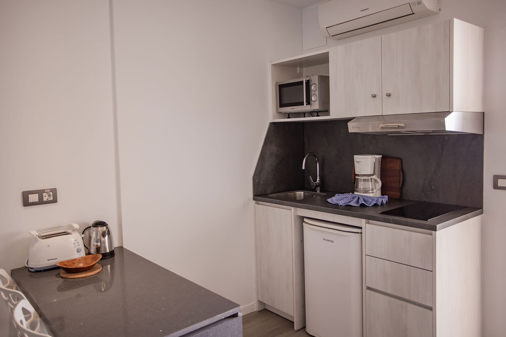 A compact kitchenette with a microwave, coffee maker, toaster, and a small refrigerator.