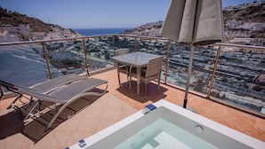 Eine Dachterrasse mit Whirlpool, Liegestühlen und einem Tisch mit Stühlen.