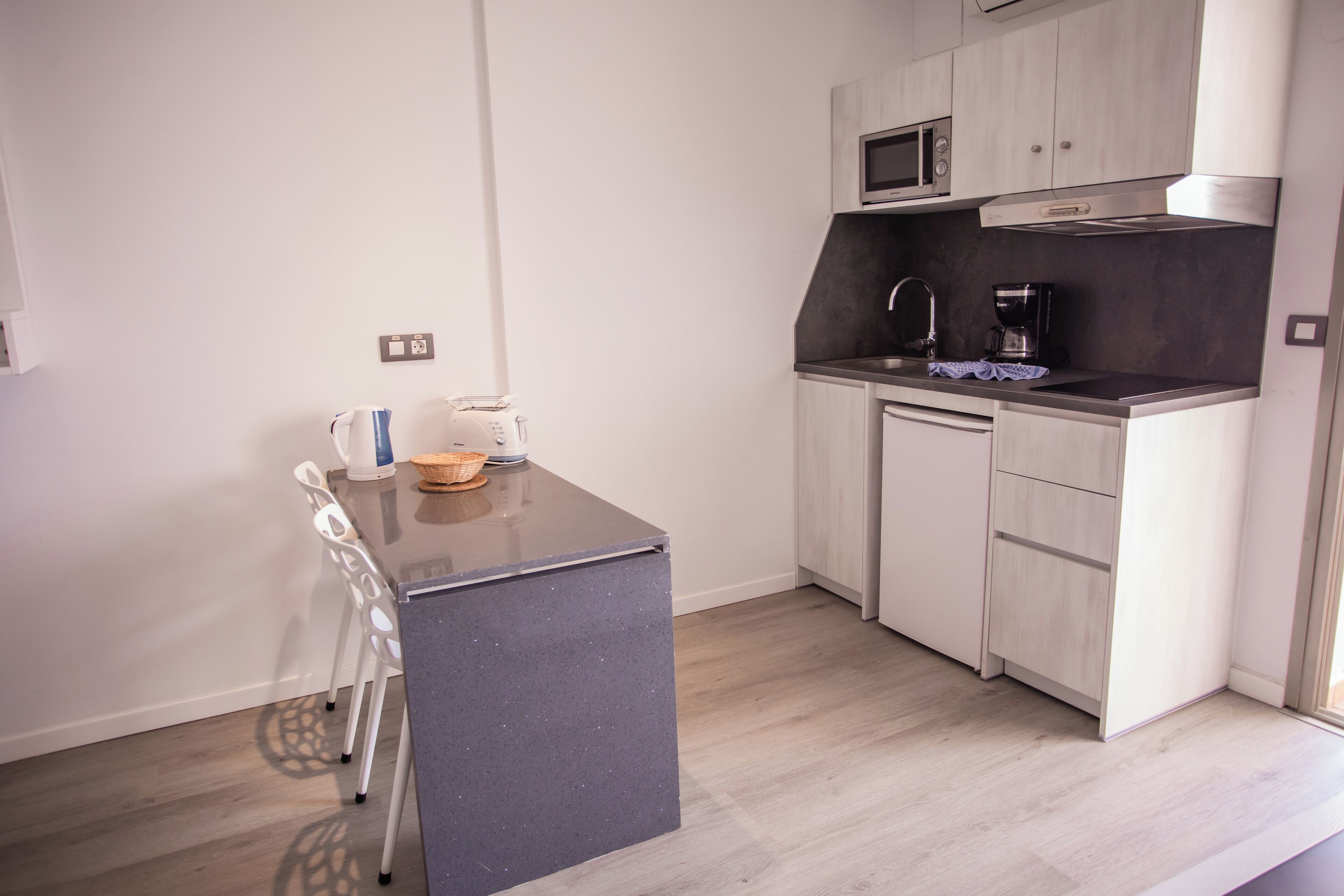 Una cucina compatta con un piano di lavoro scuro, mobili bianchi e un forno a microonde.