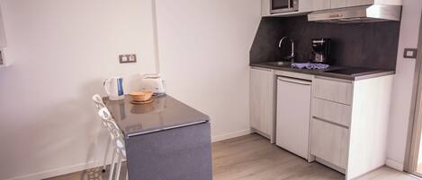 Una cucina compatta con un piano di lavoro scuro, mobili bianchi e un forno a microonde.