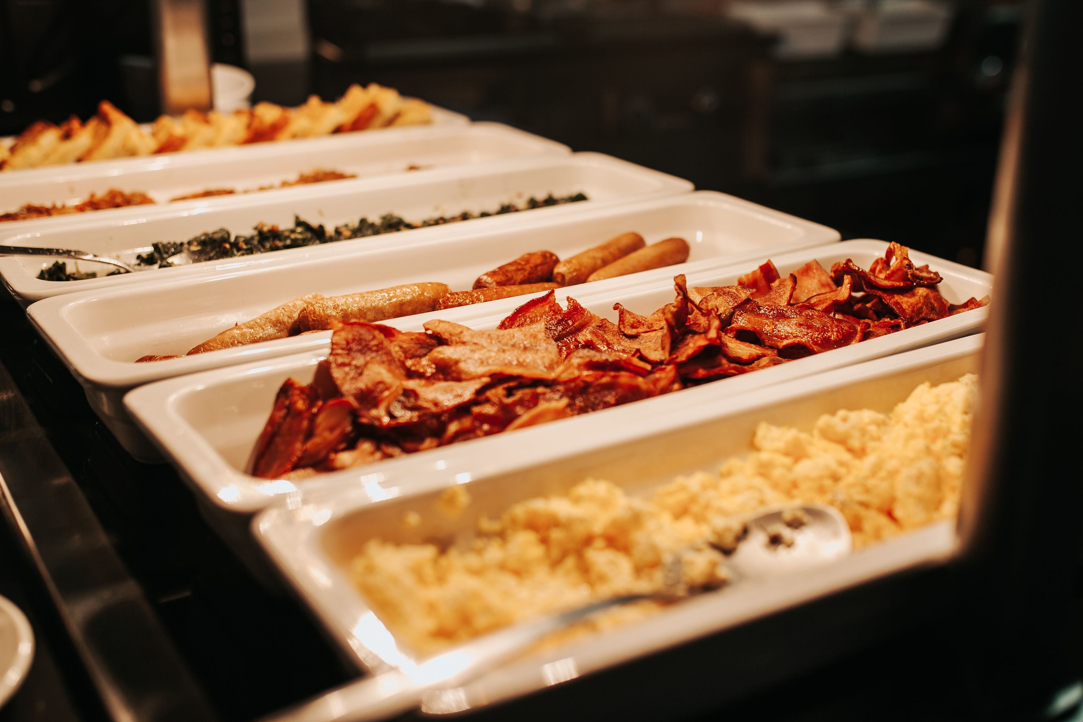 A buffet with various dishes including bacon, eggs, and vegetables.