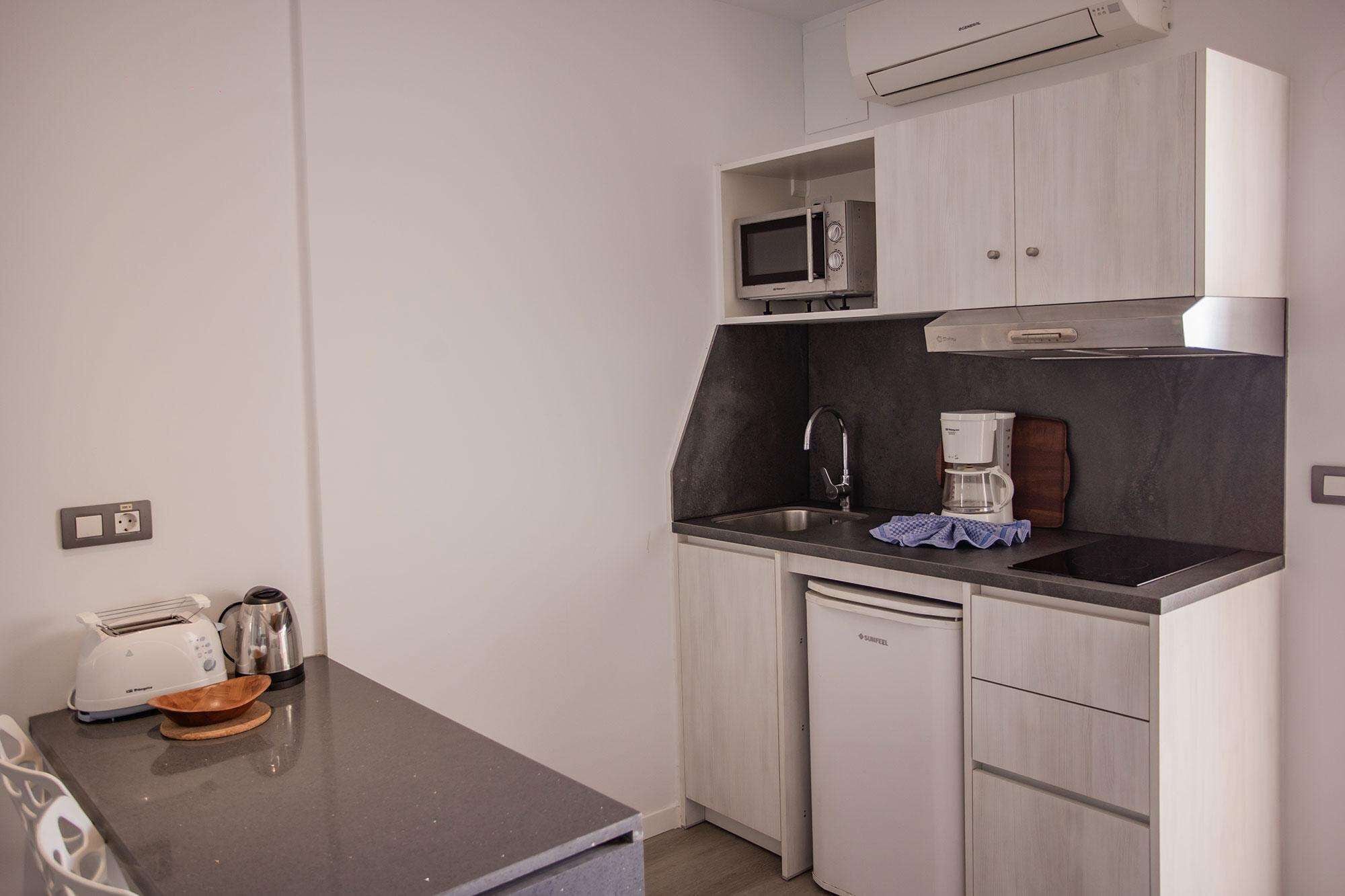 Una kitchenette compacta con microondas, cafetera y un refrigerador pequeño.