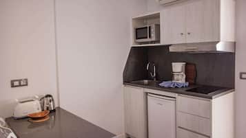 Una kitchenette compacta con microondas, cafetera y un refrigerador pequeño.