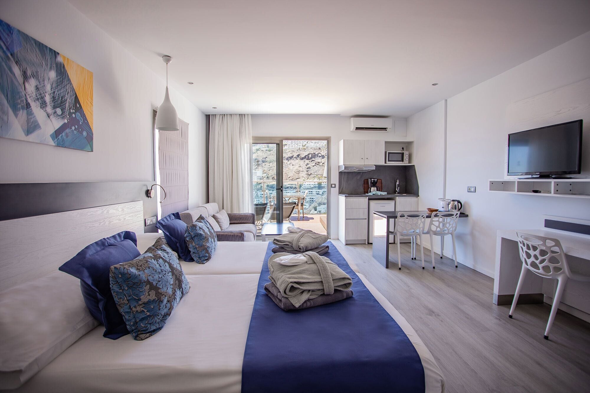 Habitación de hotel moderna con cama, escritorio, televisión y balcón con vistas.
