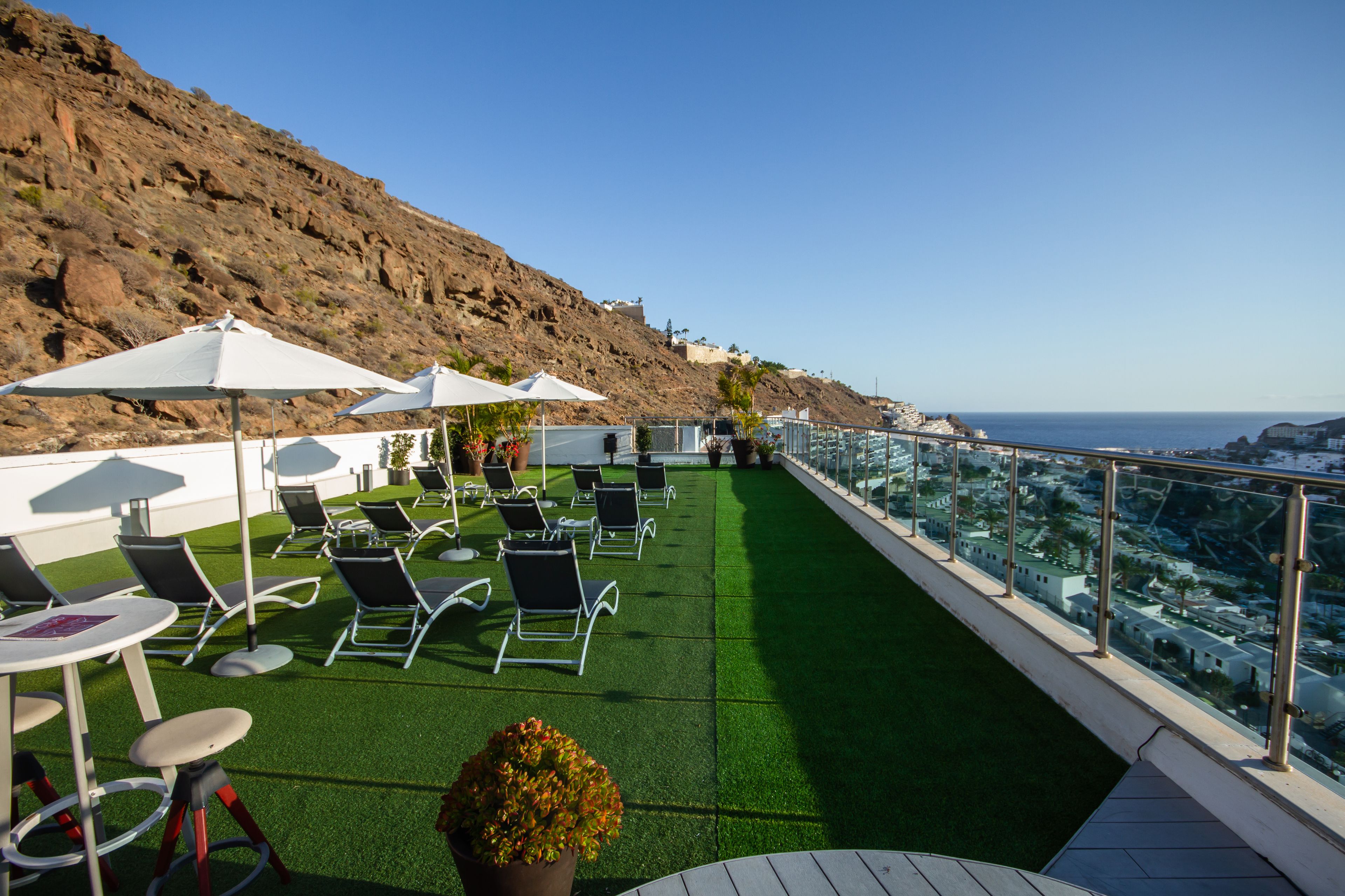 A rooftop terrace with artificial grass, outdoor seating, and a view of the coastline.
