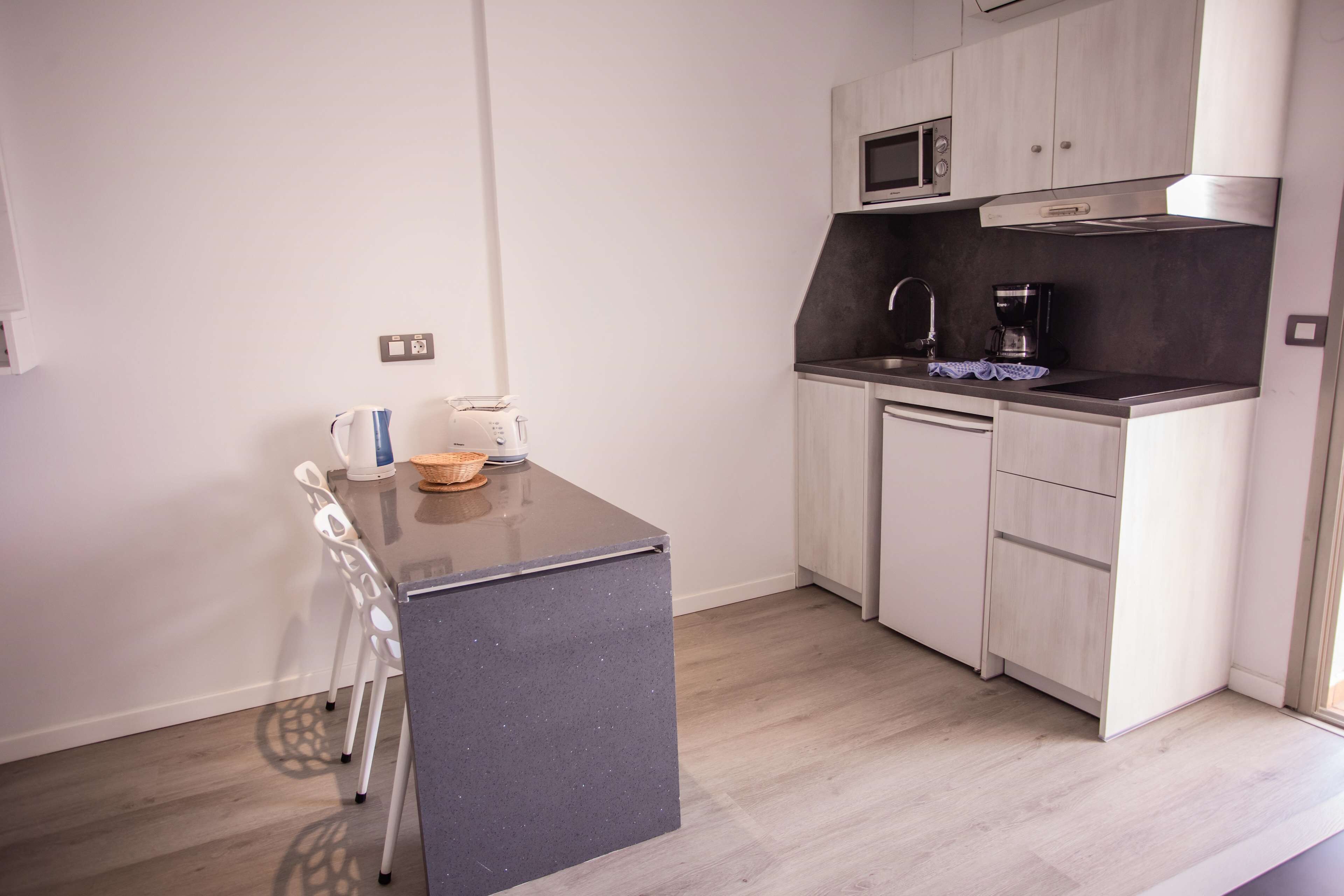 A compact kitchen with a dark countertop, white cabinets, a microwave, and a coffee maker.