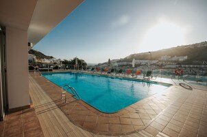 Una piscina al aire libre, sombrillas, sillones reclinables de piscina