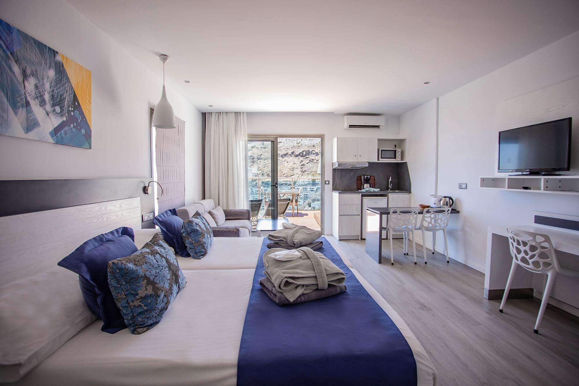 Una habitación de hotel moderna con una cama grande, un escritorio, una kitchenette y un televisor.