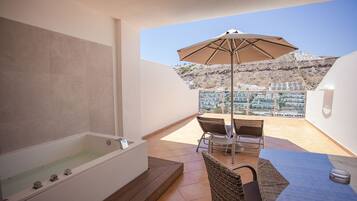 A balcony with a bathtub, a table with chairs, and an umbrella.