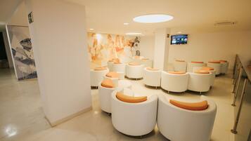 Un espace d’attente moderne avec des sièges circulaires blancs et des coussins orange, une grande fresque murale et un téléviseur fixé au mur.