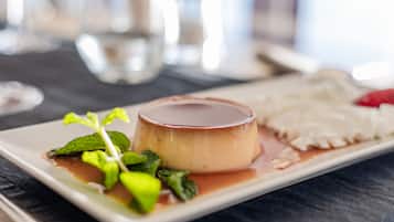 Un plato de postre con un flan de caramelo, hojas de menta y una rebanada de pastel sobre un plato blanco rectangular.