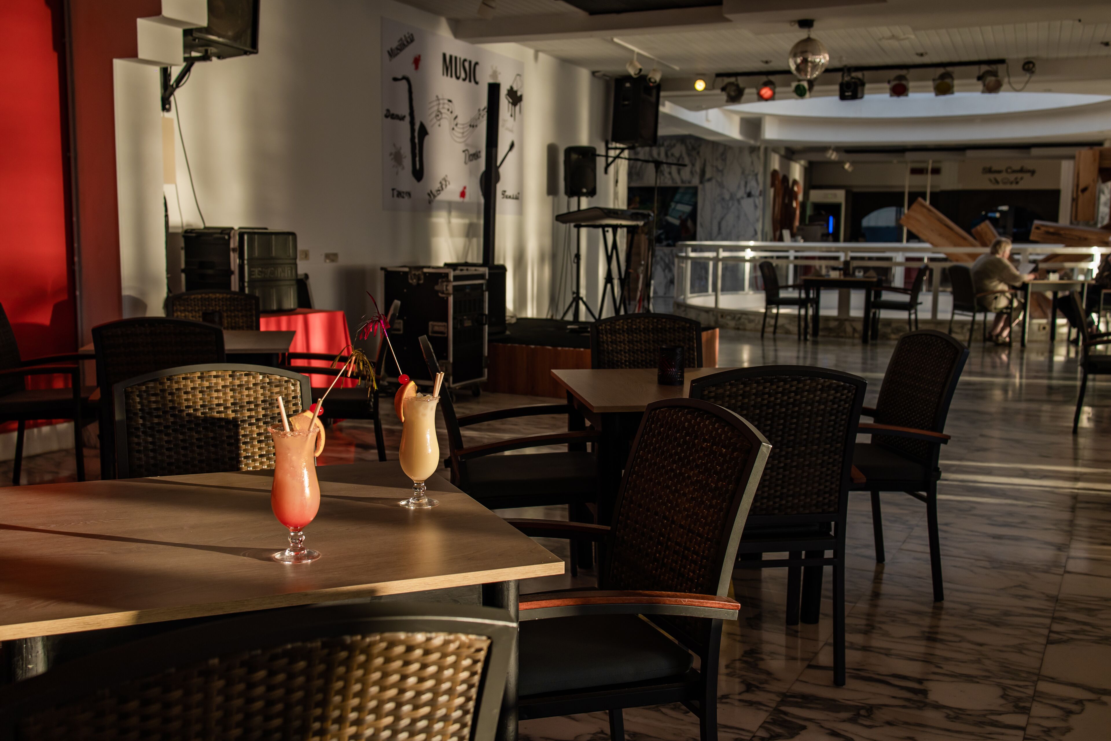 A restaurant with tables and chairs, a drink on one table, and a wall with a 'MUSIC' sign.