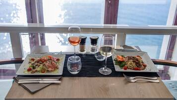 A table set with two plates of food, two wine glasses, and salt and pepper shakers.