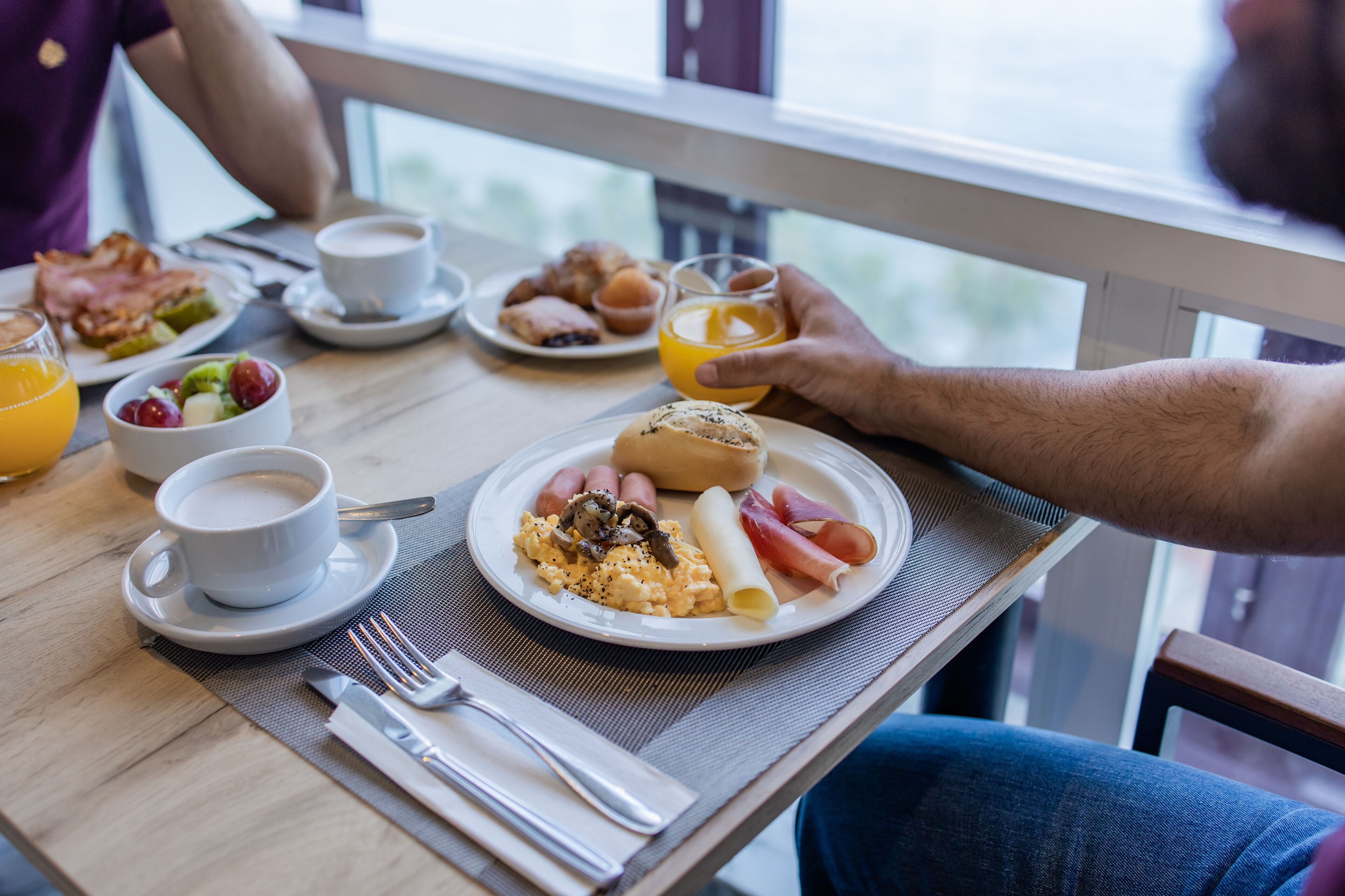 Une table de petit-déjeuner avec des assiettes remplies de nourriture, une tasse de café et un verre de jus d’orange.