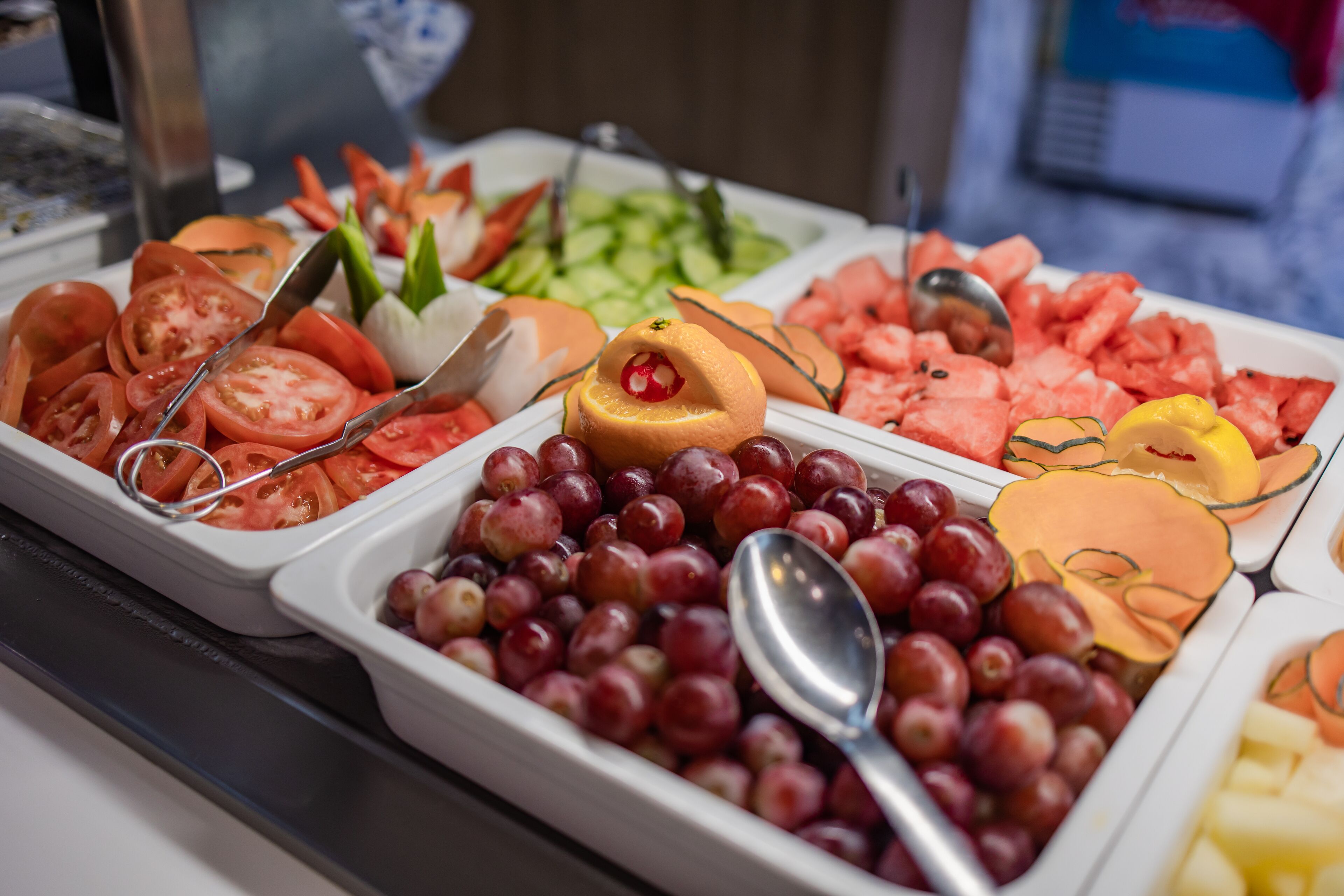 Un bufé con diversas frutas y verduras, entre ellas tomates, uvas y sandía.