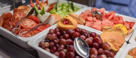 Un bufé con diversas frutas y verduras, entre ellas tomates, uvas y sandía.