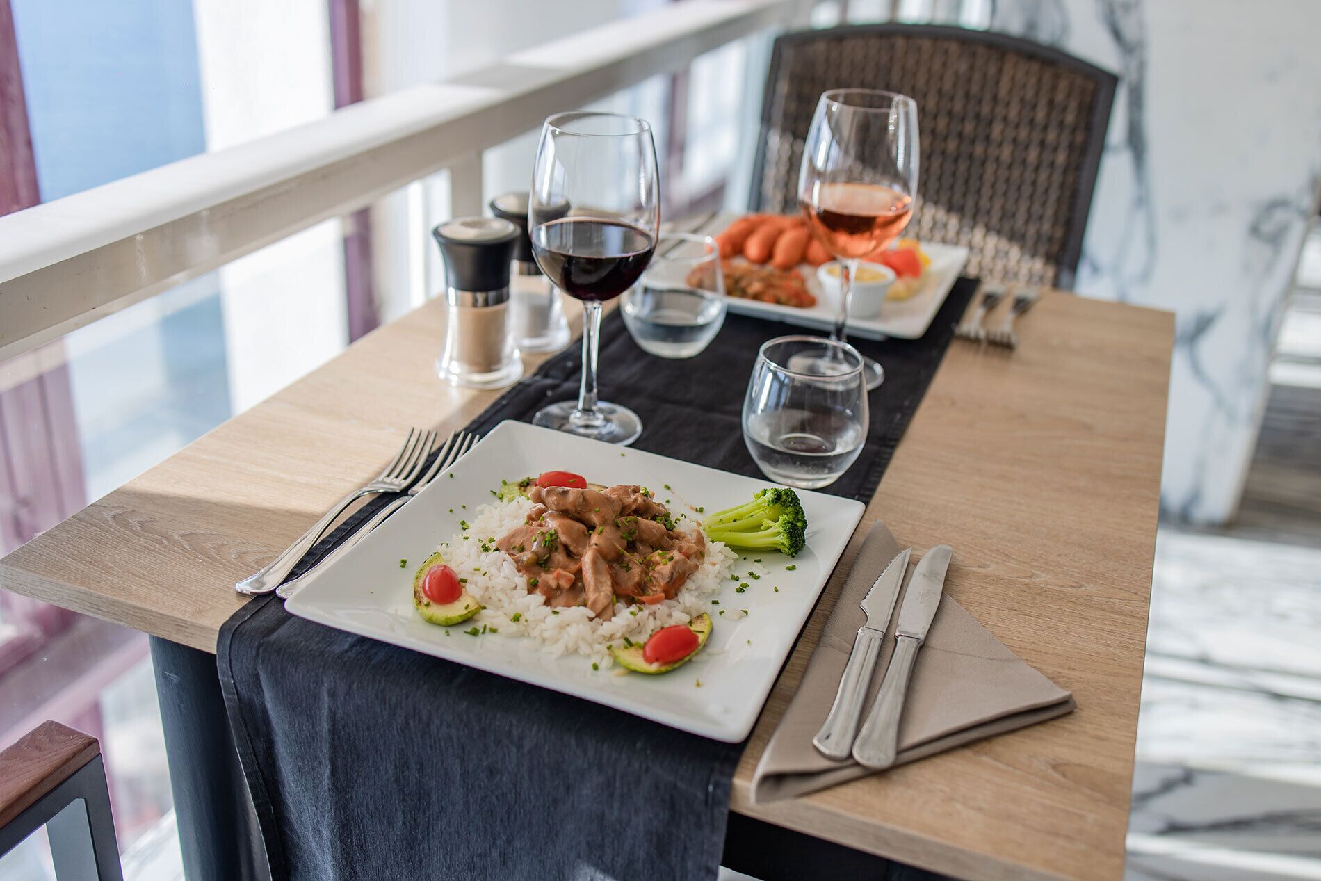 A dining table with a plate of food, a glass of red wine, and a glass of water.