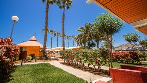 A courtyard with palm trees, a small building with a conical roof, and a clear blue sky. - Servatur Green Beach (Mogan)