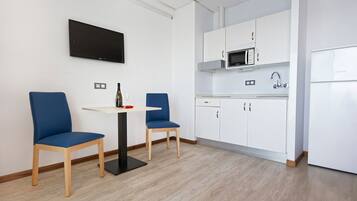 A modern kitchen with white cabinets, a microwave, and a refrigerator. There is a small dining area with two blue chairs and a table.