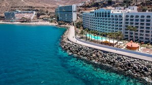 A coastal hotel with multiple buildings, a rocky shoreline, and clear blue waters. - Servatur Green Beach (Mogan)