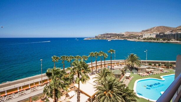 A resort with a pool, palm trees, and a view of the sea and buildings. - Servatur Green Beach (Mogan)