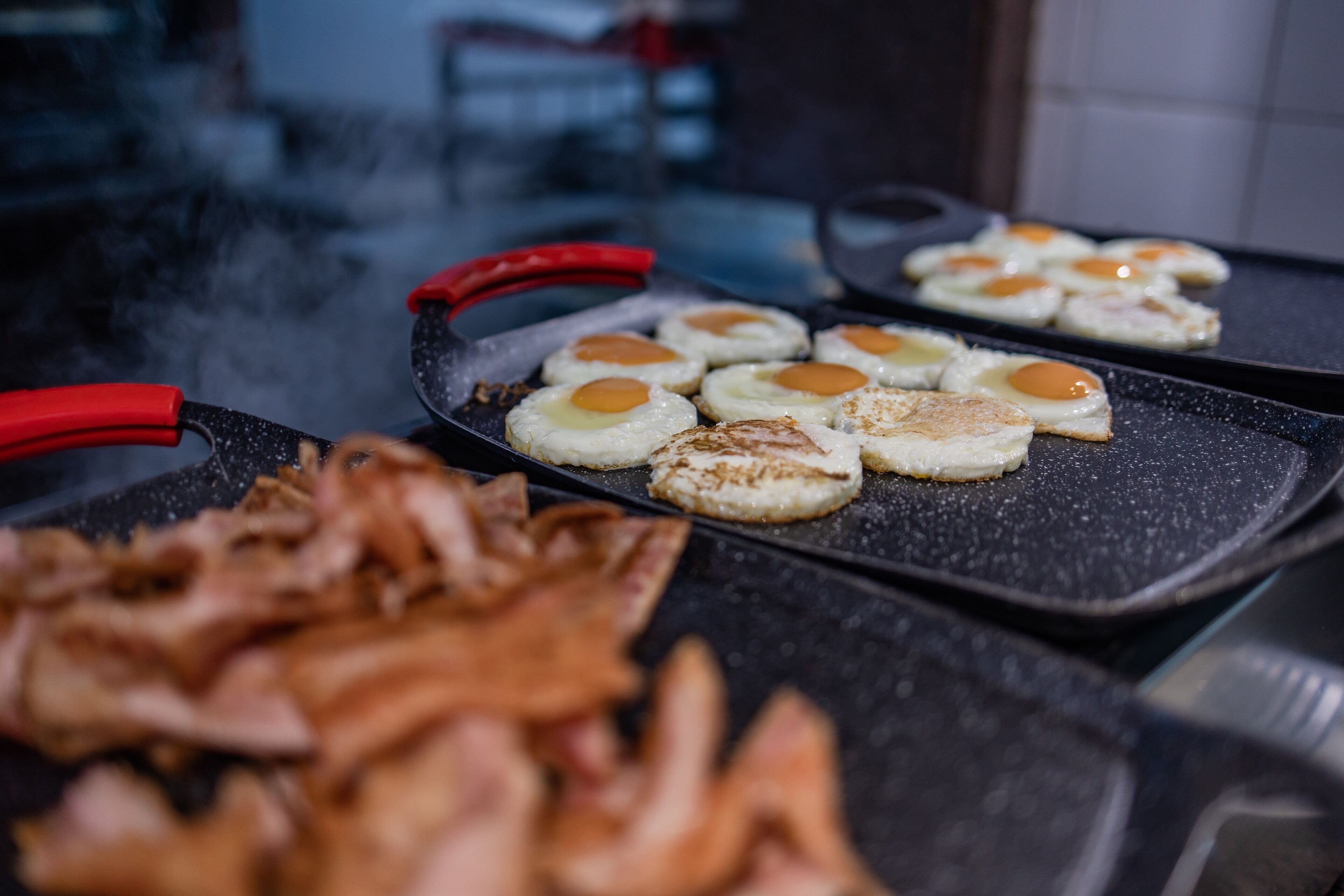 Ein Frühstücksaufbau mit Eiern und Speck auf einer Grillplatte.