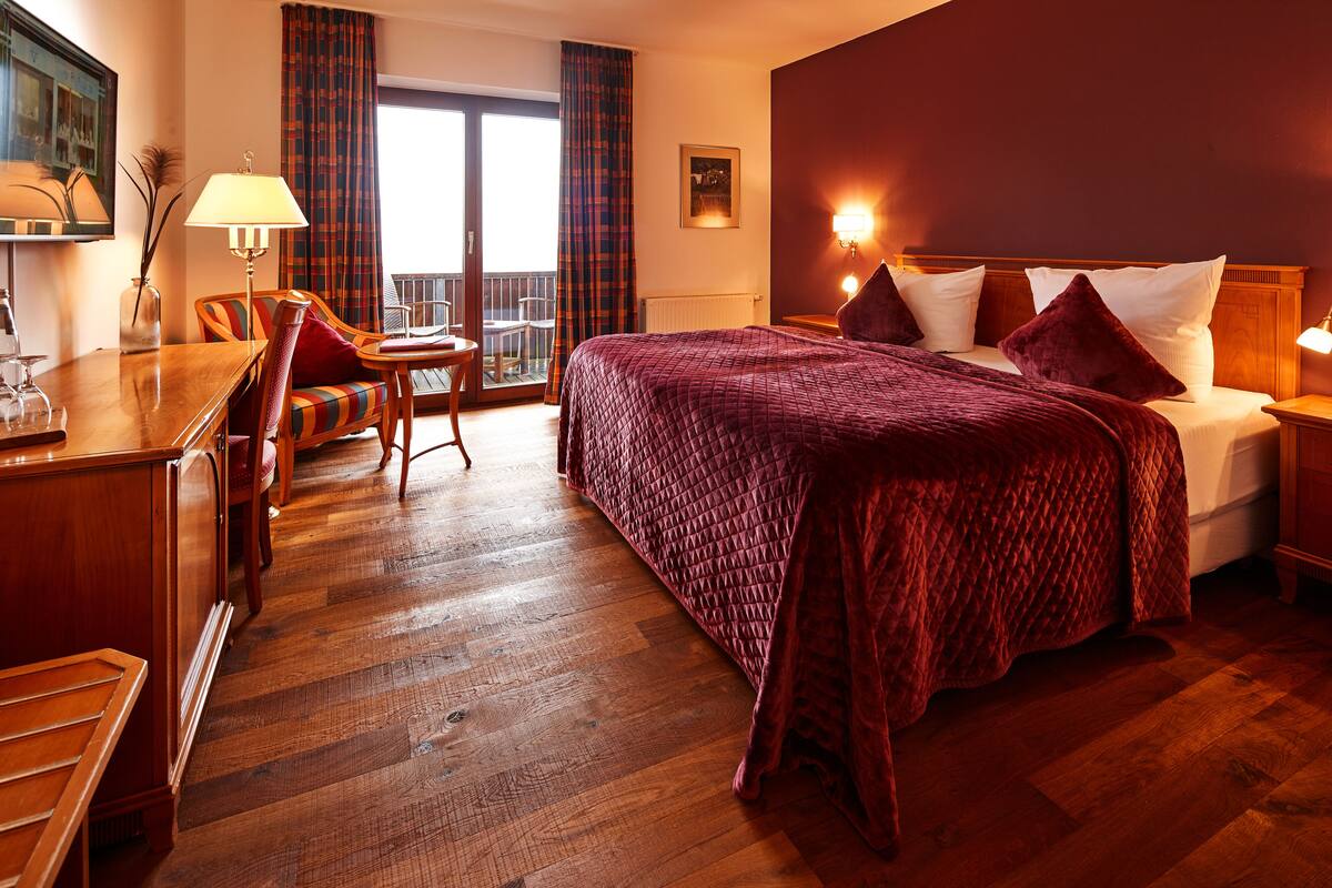 Habitación de hotel con una cama grande, un escritorio de madera, una silla, una mesa y vistas al exterior a través de una puerta corrediza.