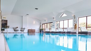 Una piscina interior moderna con agua cristalina azul, un espacio interior iluminado por el sol y sillones de descanso a orillas de la piscina.