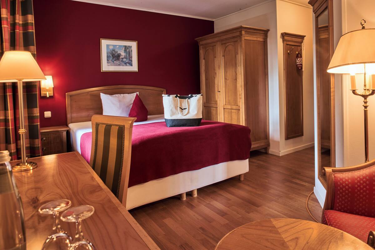 Una habitación de hotel con una cama de madera, una pared roja, un armario de madera y un suelo de madera.