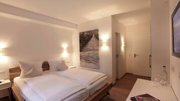 A hotel room with a bed, bedside tables, a wall-mounted TV, and a painting of a pathway.