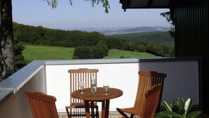 Un balcón con una mesa y sillas, con vista a un paisaje verde y colinas distantes.