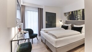 Habitación de hotel con cama, escritorio, silla, televisor y ventana con cortinas.