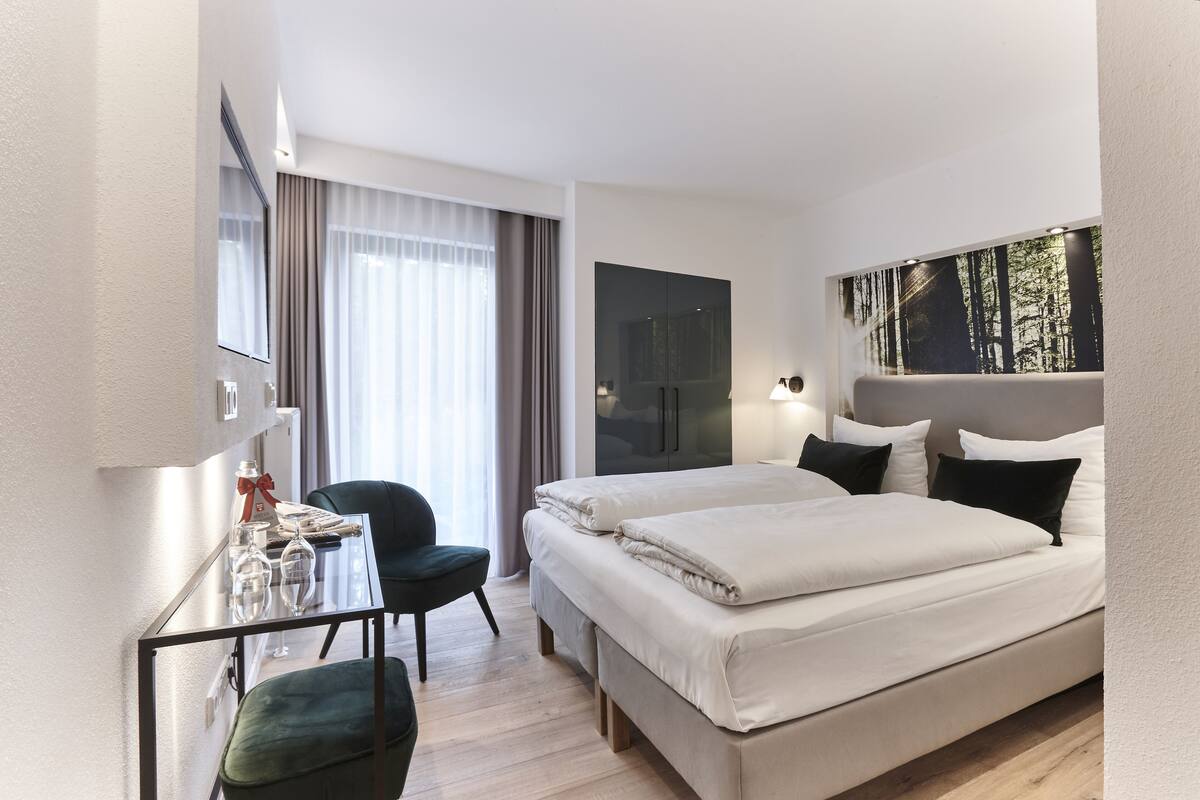 Habitación de hotel con cama, escritorio, silla, televisor y ventana con cortinas.