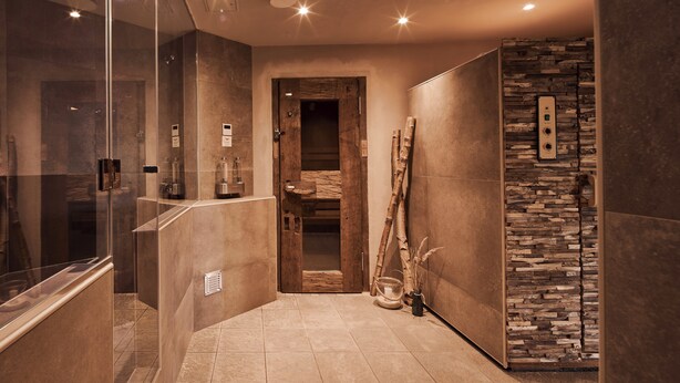 Un baño moderno con cabina de ducha de vidrio, puerta de madera y pared de acento de piedra.