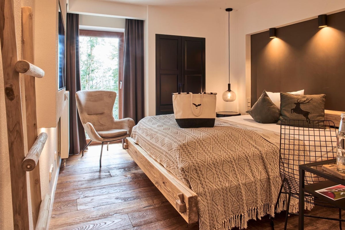 A bedroom with a wooden bed, a chair, a bedside table, and a lamp.